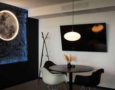 Modern room with a round table and OLYPSO pendant luminaire, two chairs, a wall-mounted TV, a coat rack, and a moon-themed wall light.
